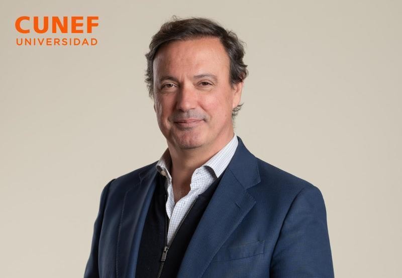 Retrato de un hombre sonriendo, vestido con blazer y camisa, frente a un fondo neutro.